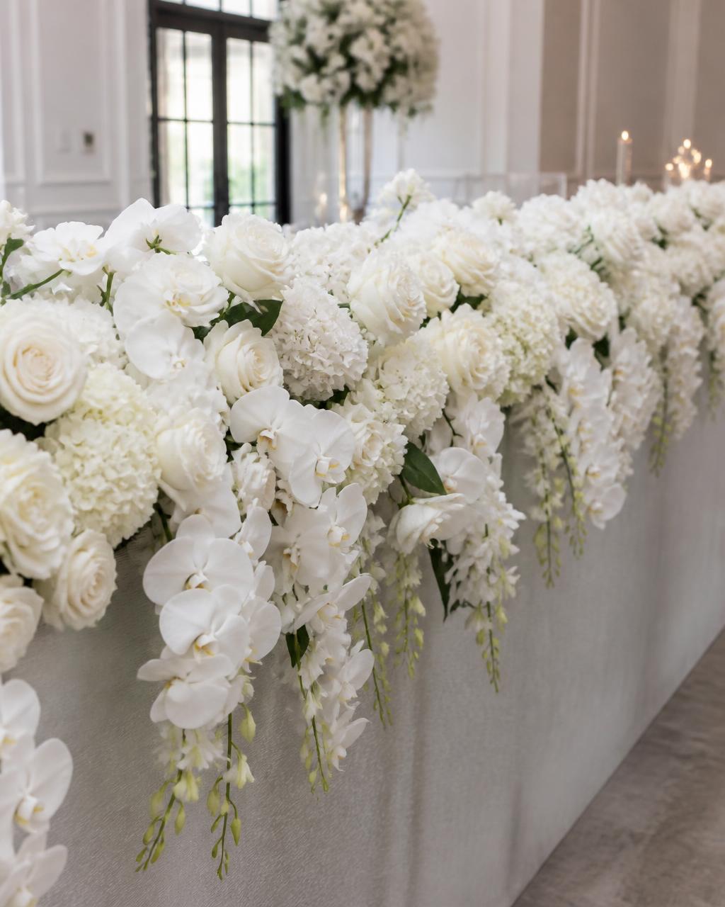 Modern white floral installation cascading over a reception table at an elegant indoor event